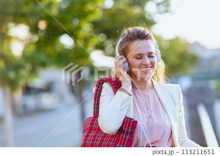 happy stylish woman in city listening to music with headphones 113211651