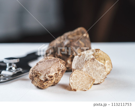 Expensive black truffles gourmet mushrooms on white table in restaurant interior. Row of brown truffles with slice on a white table with dark background. Truffle mushrooms is culinary delight. Close 113211753