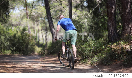 Young man riding bicycle along path of park back view 113212490