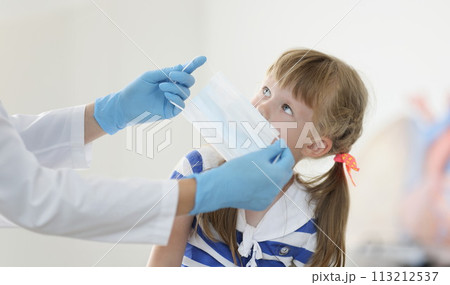 Doctor putting protective medical mask on little girl in clinic Doctor putting protective medical mask on little girl in clinic 113212537