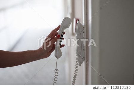 Woman hand picking up phone in hotel corridor closeup 113213180