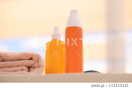 Two orange bottles with sunscreen lying on beach near towels closeup Two orange bottles with sunscreen lying on beach near towels closeup 113213181