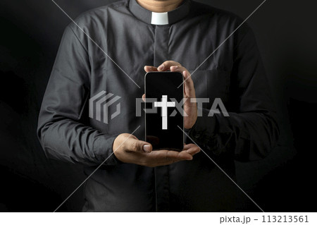 Young priest holding smartphone with image of cross isolated on black background. Young priest holding smartphone with image of cross isolated on black background. 113213561