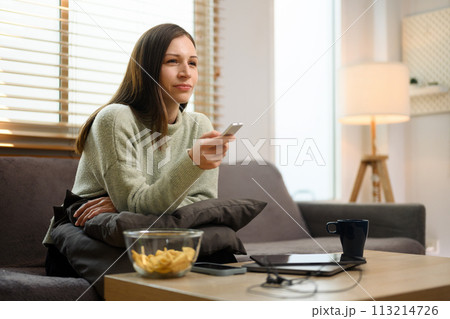 Beautiful caucasian woman with remote control watching television at home Beautiful caucasian woman with remote control watching television at home 113214726