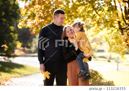 Family day. Young dad, mom holds adorable little child daughter in hands enjoying spend time together at weekend outdoor at autumn park, kid kisses mommy. Parental love, mental health. Happy childhood 113216355