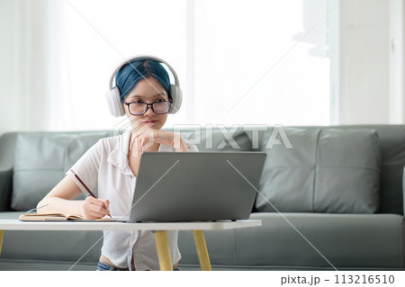 Happy young woman teenage wearing headphones writing note. student online learning class study online video call zoom teacher with laptop and book 113216510