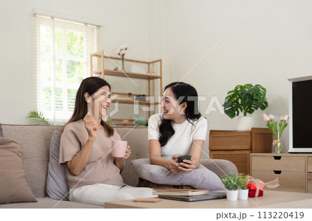 Happy senior mother with adult daughter sitting on couch and holding cups with coffee or tea at home. Enjoy family concept 113220419