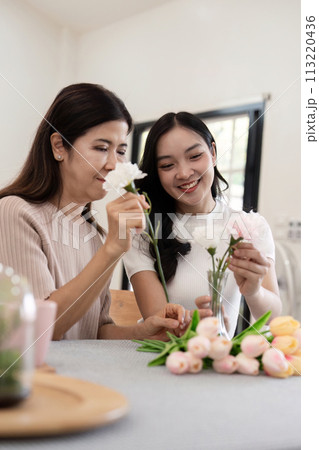 Senior mother and adult daughter happy on the table while arrange flowers in a vase together. Technology and lifestyle concept. Happy time together 113220436