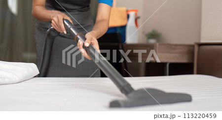 Cleaning service employee removing dirt from with professional equipment. Female housekeeper cleaning the mattress on the bed with vacuum cleaner Cleaning service employee removing dirt from with professional equipment. Female housekeeper cleaning the mattress on the bed with vacuum cleaner 113220459