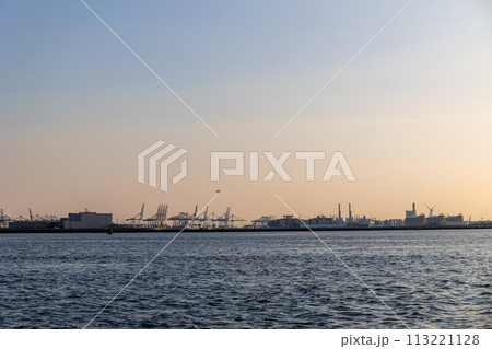 Ships float across the North Sea. Windmills in the background. Sea port in the Netherlands. A lot of cranes for loading goods. Different ships and barges. 113221128