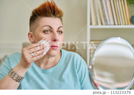 Middle-aged woman with a mirror taking care of her facial skin Middle-aged woman with a mirror taking care of her facial skin 113223379