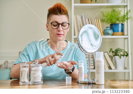 Middle-aged woman with a mirror taking care of her facial skin Middle-aged woman with a mirror taking care of her facial skin 113223380