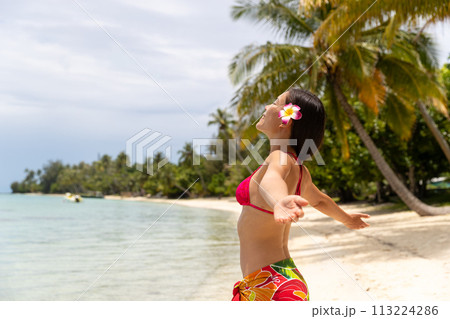 Happy free summer vacation beach bikini body woman enjoying sun carefree with open arms sunbathing at paradise beach in skirt and flower. Image is unretouched and model without makeup. Raw Image Happy free summer vacation beach bikini body woman enjoying sun carefree with open arms sunbathing at paradise beach in skirt and flower. Image is unretouched and model without makeup. Raw Image 113224286