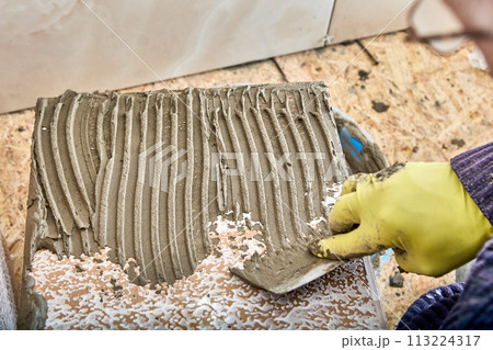 Cement mortar of tile adhesive is applied to tiles using notched trowel. 113224317