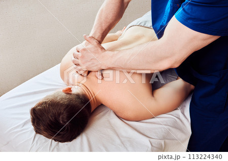 Massage therapist kneads back muscles in area of shoulder blade of male patient. Massage therapist kneads back muscles in area of shoulder blade of male patient. 113224340