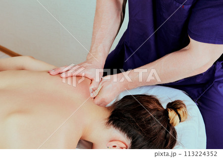 White woman receives physiotherapy treatments lying face down on massage table, European female in her 20s, at masseuse appointment. White woman receives physiotherapy treatments lying face down on massage table, European female in her 20s, at masseuse appointment. 113224352
