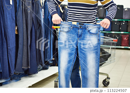 Man chooses blue jeans in shop Man chooses blue jeans in shop 113224507
