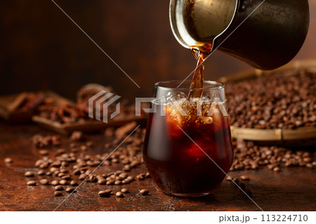 Black iced coffee with coffee beans on a brown vintage table. Black iced coffee with coffee beans on a brown vintage table. 113224710