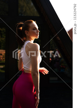 Vertical side view of sporty female athlete preforming fitness training session at country house building exterior. Healthy woman warming up outdoors on summer morning. Concept of wellness, fitness Vertical side view of sporty female athlete preforming fitness training session at country house building exterior. Healthy woman warming up outdoors on summer morning. Concept of wellness, fitness 113224792