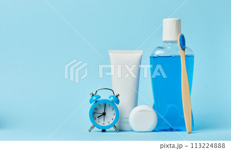 Mouthwash and toothpaste tube, alarm clock on blue background 113224888
