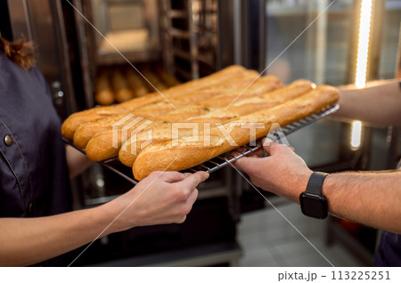 Unrecognizable bakers holding tray with fresh baked baguettes 113225251