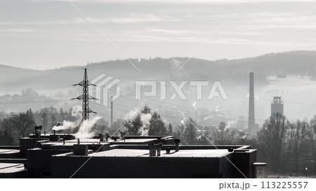 Smoke rises from chimneys against a backdrop of hazy hills, as smog blankets an industrial town at dawn, highlighting environmental concerns. 113225557