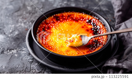 A classic Creme brulee, served in a ramekin, with a spoon breaking through the caramelized surface of the dessert. 113225591