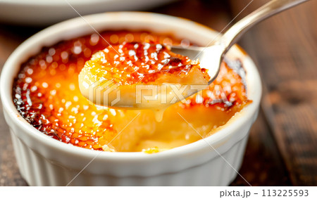 A classic Creme brulee, served in a ramekin, with a spoon breaking through the caramelized surface of the dessert. 113225593