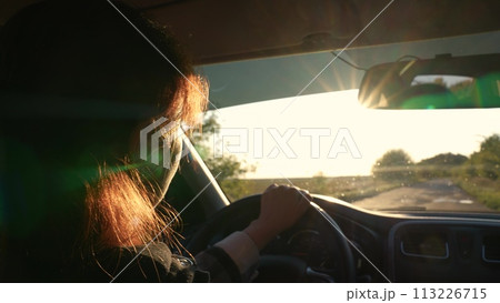 Female driver riding on asphalt road trip at countryside rural scenery with bright sun closeup back view. Active woman driving automobile at summer landscape path mobility weekend travel adventure Female driver riding on asphalt road trip at countryside rural scenery with bright sun closeup back view. Active woman driving automobile at summer landscape path mobility weekend travel adventure 113226715