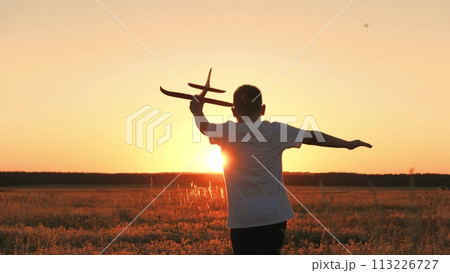 boy runs with plane his hand, child boy plays with toy plane, child son runs happily through field sunset, fantastic dream airplane pilot, cheerful child boy runs happily with toy plane through park 113226727