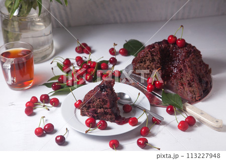 Chocolate cake with sweet cherry, cup of tea and bouquet of blue flowers on white background.. 113227948