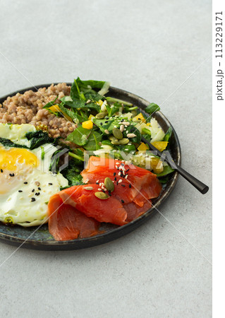 Buckwheat with fried egg and salmon fish, mix salad with fresh herbs and peppers 113229171