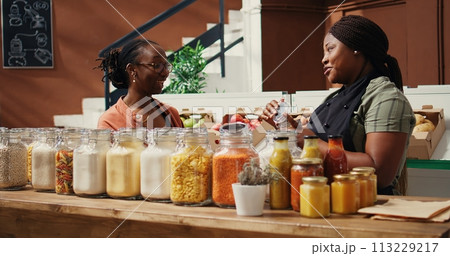 African american seller giving food sample to customer, presenting new homemade snacks with natural ingredients. Vegan woman trying out market products before buying. Handheld shot. African american seller giving food sample to customer, presenting new homemade snacks with natural ingredients. Vegan woman trying out market products before buying. Handheld shot. 113229217