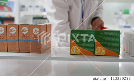 POV of druggist taking nutritional vitamins boxes from shelves, replacing them with other medication. Employee rearranging pharmaceutical products in healthcare facility. Tripod shot. 113229258