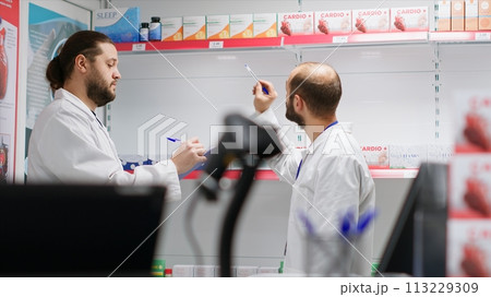 Team of pharmacists ensuring products stock in a drugstore, counting all medicaments and dietary supplements on shelves. Pharmacy staff members working together to do inventory. 113229309