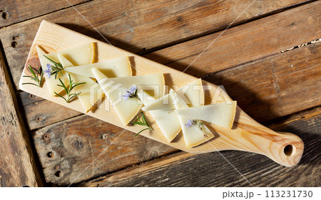 Delicious cheese slices served with rosemary sprouts and flowers on wooden cutting board 113231730