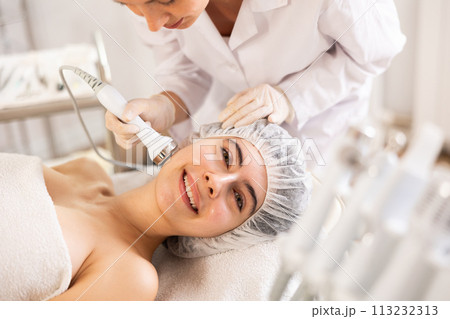 Young female cosmetologist doing ultrasound procedure to young woman Young female cosmetologist doing ultrasound procedure to young woman 113232313