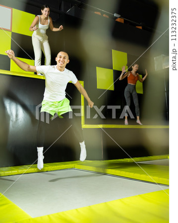 Joyful young man jumping on trampolines in colorful amusement park 113232375