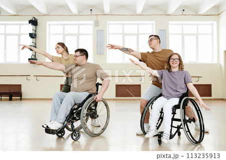 Group of four cheerful diverse people practicing modern dance with wheelchairs in spacious hall Group of four cheerful diverse people practicing modern dance with wheelchairs in spacious hall 113235913