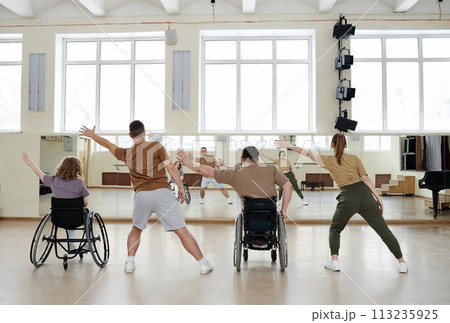 Rear view of four diverse men and women practicing dance with wheelchairs in front of mirrors in studio, long shot Rear view of four diverse men and women practicing dance with wheelchairs in front of mirrors in studio, long shot 113235925