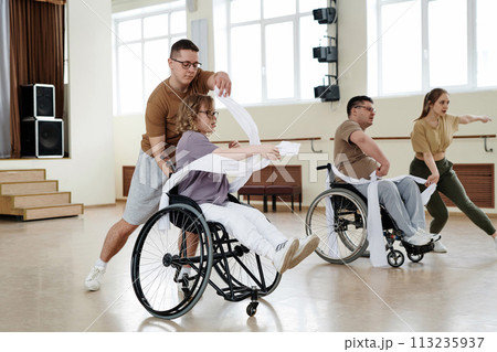 Group of four diverse men and women practicing dance with wheelchairs in studio, long shot 113235937