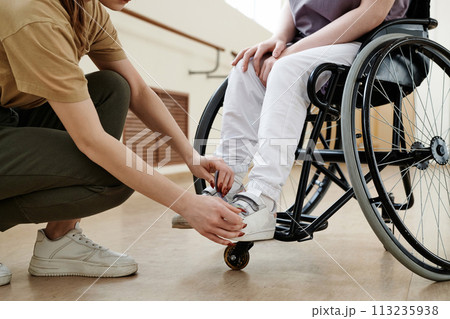 Crop shot of unrecognizable dance coach helping woman in wheelchair to fix shoes on her feet Crop shot of unrecognizable dance coach helping woman in wheelchair to fix shoes on her feet 113235938