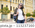 A female pedestrian strolling on the street while holding a beverage in her hand. 113237160