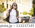 A woman strolling along a busy street while carrying a beverage in her hand. 113237185