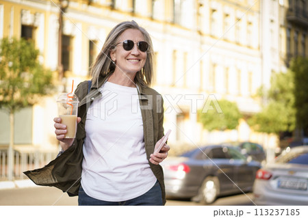 A woman strolling along a busy street while carrying a beverage in her hand. 113237185