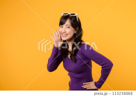 Portrait young beautiful 30s asian woman happy smile dressed in purple clothes shout to free space isolated on yellow studio background. Presenting product Beautiful girl act like telling to customer. 113238868