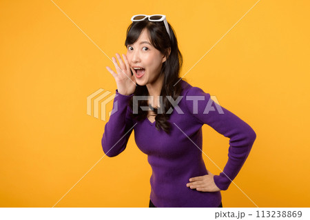 Portrait young beautiful asian woman 30s happy smile dressed in purple clothes shout to free space isolated on yellow studio background. Presenting product Beautiful girl act like telling to customer 113238869