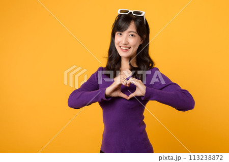 Expressing love and happiness on Valentine's Day, a cheerful young woman forms a heart shape with her hand in a studio portrait, symbolizing romance. 113238872