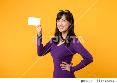 Against a vibrant yellow backdrop, a modern woman, in purple shirt and sunglasses, showcases an empty card, a blank slate for your message. 113238893