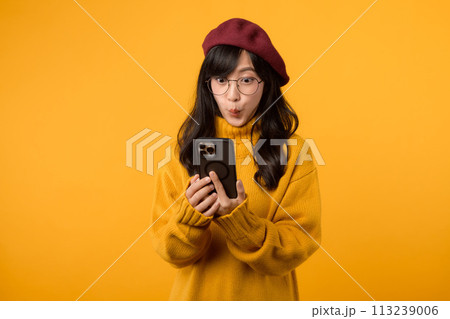 Portrait young Asian woman 30s wearing yellow shirt and glasses receive an exited news from mobile phone isolated on yellow background. Great news concept. 113239006